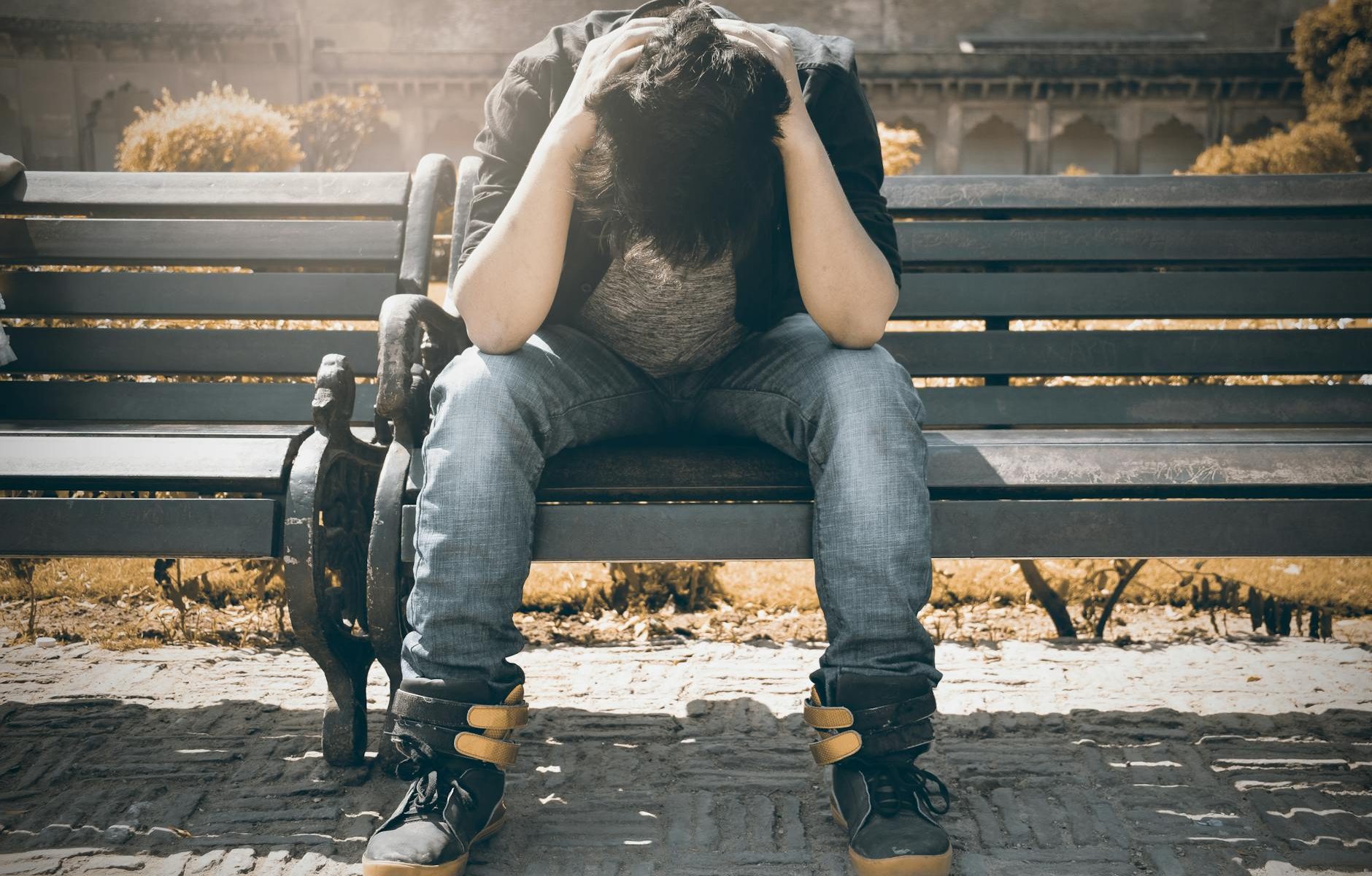 man in black shirt and gray denim pants sitting on gray padded bench