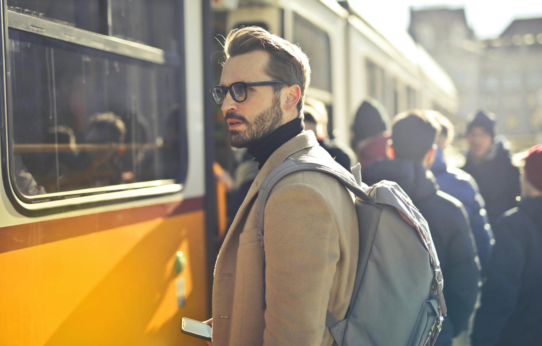 man in brown coat and gray backpack posing for a photo